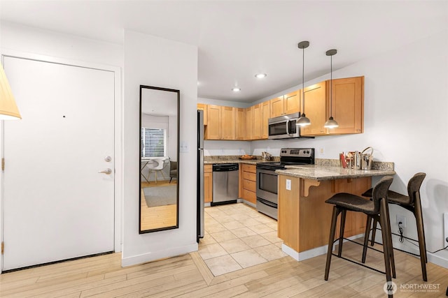 kitchen with appliances with stainless steel finishes, a peninsula, a breakfast bar area, light wood finished floors, and dark stone counters
