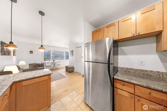 kitchen with freestanding refrigerator, open floor plan, light wood-type flooring, light stone countertops, and hanging light fixtures
