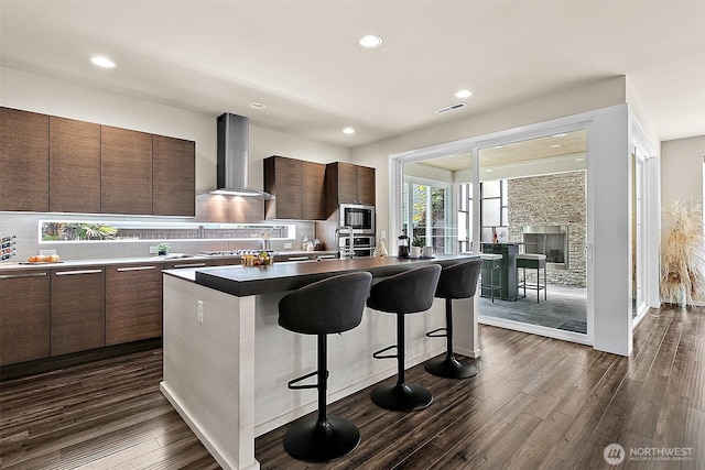 30429 121st Pl SE, Auburn, WA 98092 - kitchen with wall chimney range hood, modern cabinets, appliances with stainless steel finishes, a kitchen bar, and dark wood finished floors