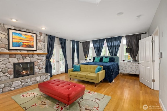 bedroom with access to outside, wood finished floors, and a stone fireplace