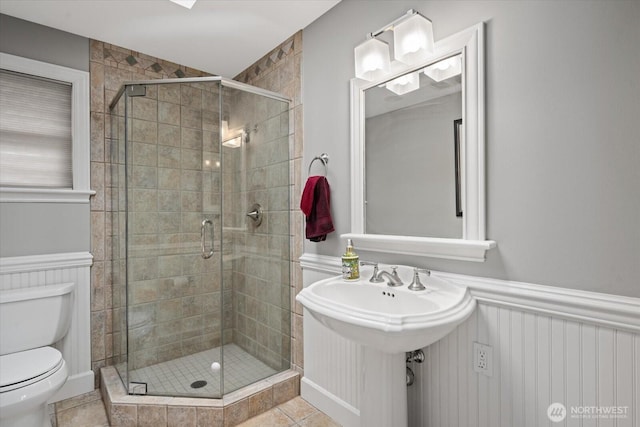 bathroom with toilet, a shower stall, a wainscoted wall, and tile patterned floors