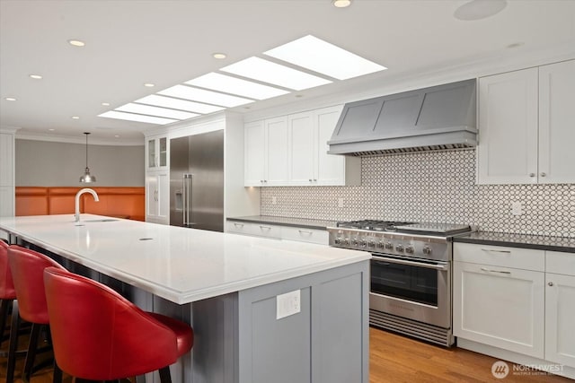 kitchen featuring high end appliances, custom exhaust hood, crown molding, a sink, and a kitchen bar