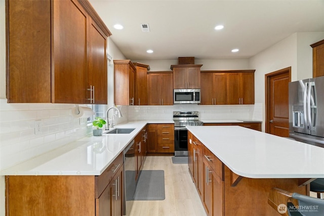 kitchen featuring appliances with stainless steel finishes, a sink, a center island, recessed lighting, and tasteful backsplash