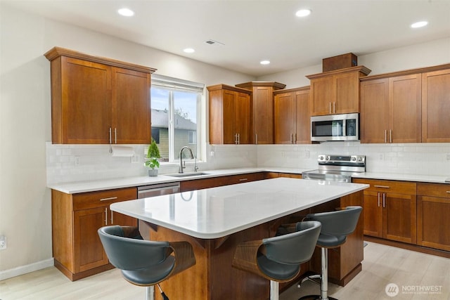 kitchen with stainless steel appliances, a sink, a breakfast bar, brown cabinets, and light countertops