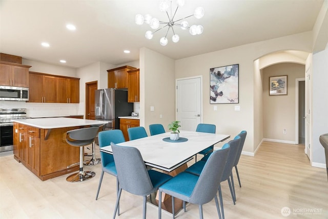 dining space featuring light wood finished floors, arched walkways, recessed lighting, baseboards, and a chandelier