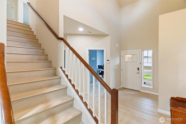 entryway with stairs, wood finished floors, baseboards, and a high ceiling