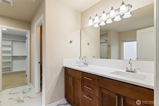 bathroom featuring marble finish flooring, baseboards, a spacious closet, double vanity, and a stall shower