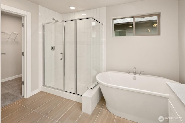 bathroom featuring a stall shower, a freestanding tub, a walk in closet, recessed lighting, and baseboards