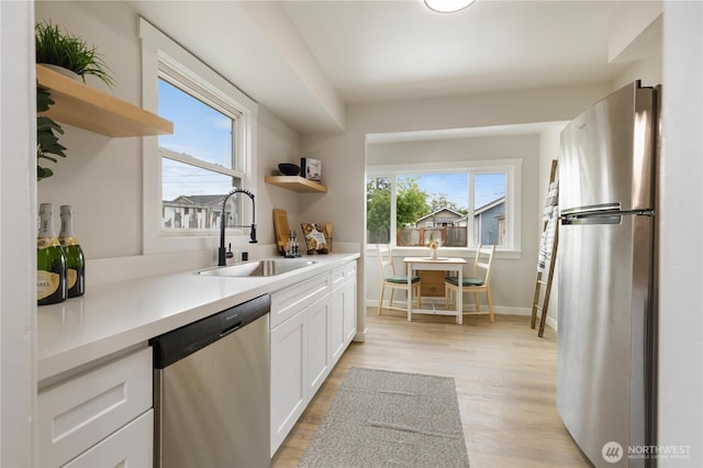 kitchen featuring stainless steel appliances, open shelves, a sink, white cabinets, and light wood finished floors