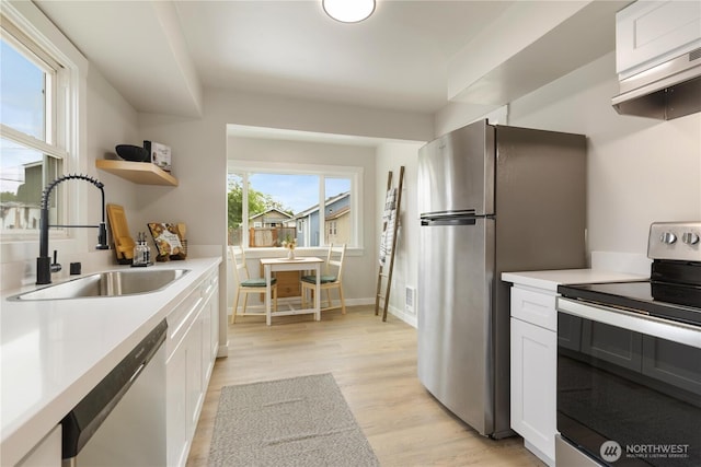 kitchen with stainless steel appliances, a sink, light wood finished floors, white cabinets, and light countertops