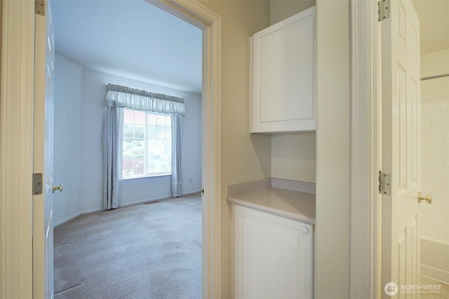corridor featuring light colored carpet and baseboards