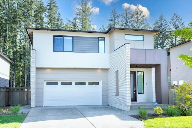 contemporary home with an attached garage, concrete driveway, and fence