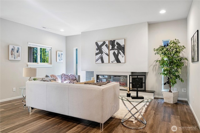 living room with a glass covered fireplace, dark wood finished floors, recessed lighting, and baseboards