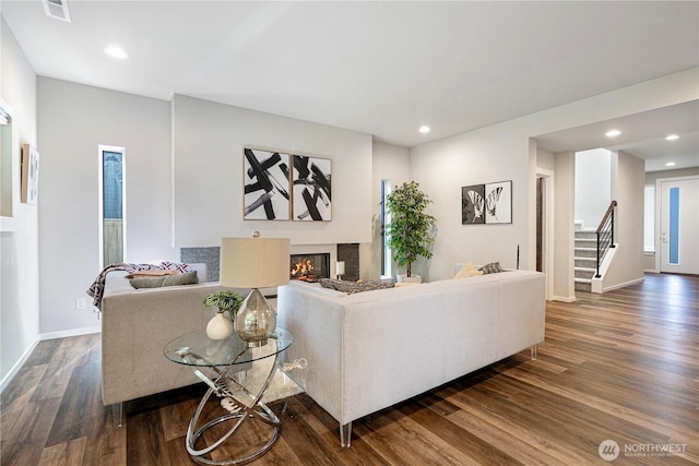 living area featuring dark wood finished floors, stairs, a glass covered fireplace, baseboards, and recessed lighting