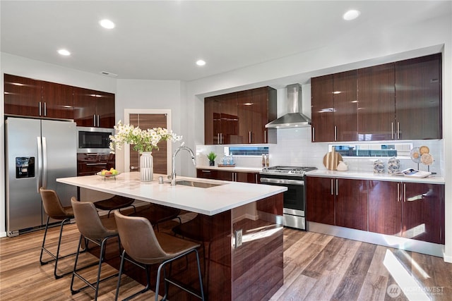 kitchen with appliances with stainless steel finishes, wall chimney range hood, a sink, modern cabinets, and recessed lighting