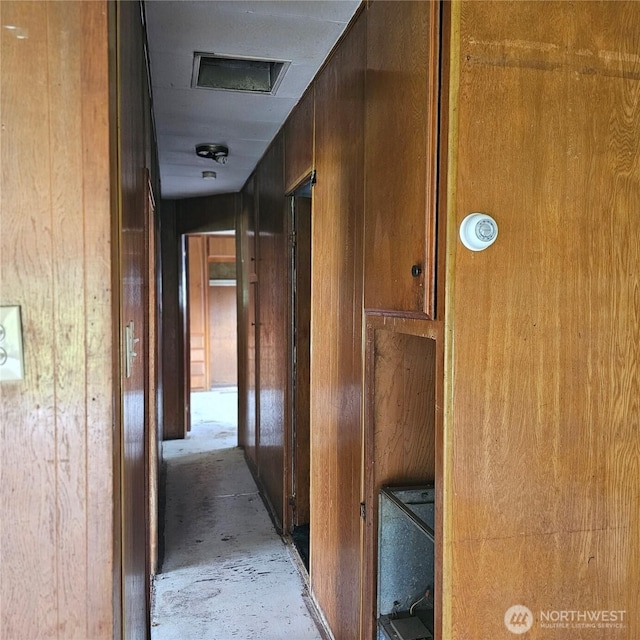 hallway featuring wooden walls and unfinished concrete flooring