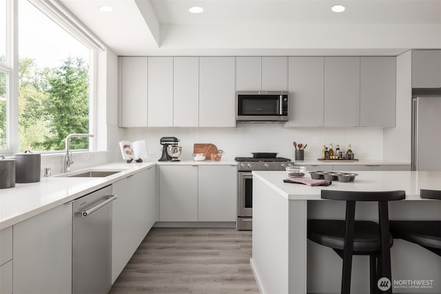 kitchen featuring stainless steel appliances, a breakfast bar, a sink, decorative backsplash, and light countertops