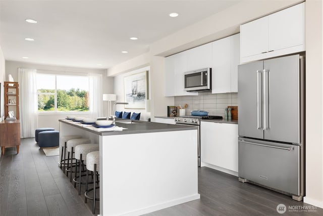 kitchen with appliances with stainless steel finishes, dark wood-type flooring, a sink, white cabinetry, and tasteful backsplash