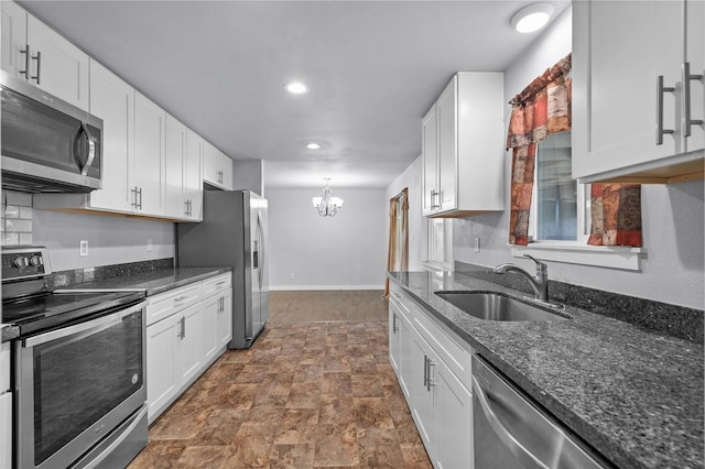 kitchen with appliances with stainless steel finishes, a sink, stone finish floors, a chandelier, and white cabinets