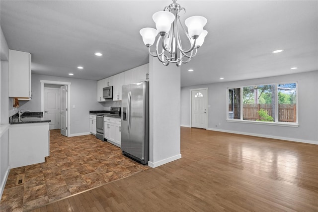 kitchen featuring appliances with stainless steel finishes, dark countertops, a sink, white cabinetry, and recessed lighting