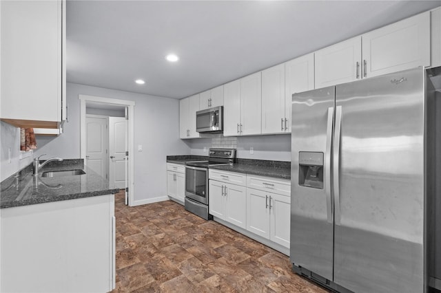 kitchen with appliances with stainless steel finishes, a sink, recessed lighting, white cabinetry, and dark stone countertops