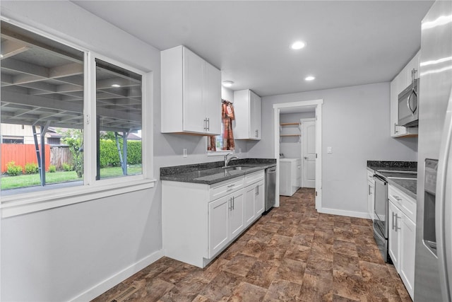 kitchen with stainless steel appliances, baseboards, white cabinetry, a sink, and washer and clothes dryer