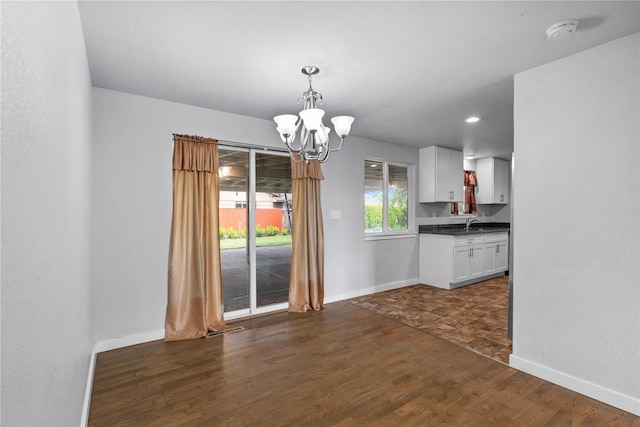 unfurnished dining area featuring dark wood-type flooring, a chandelier, and baseboards