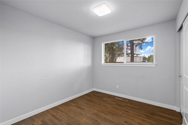unfurnished room with baseboards and dark wood-type flooring