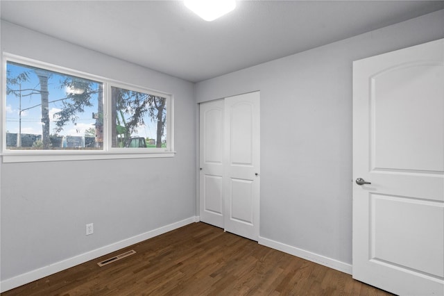 unfurnished bedroom featuring baseboards, dark wood-type flooring, and a closet