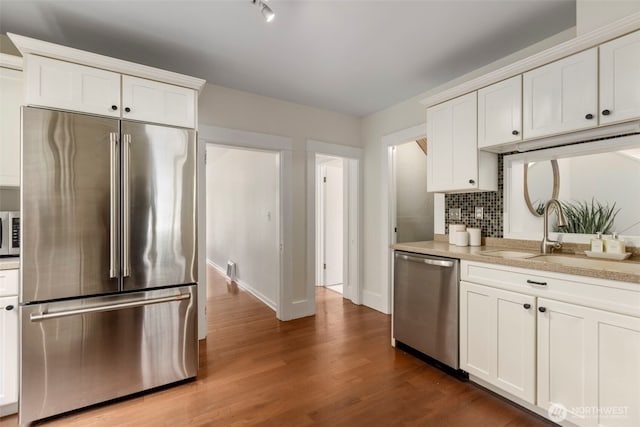 kitchen with stainless steel appliances, a sink, decorative backsplash, light countertops, and white cabinets