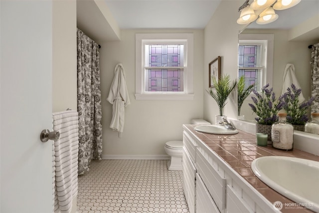 full bathroom with toilet, double vanity, and baseboards