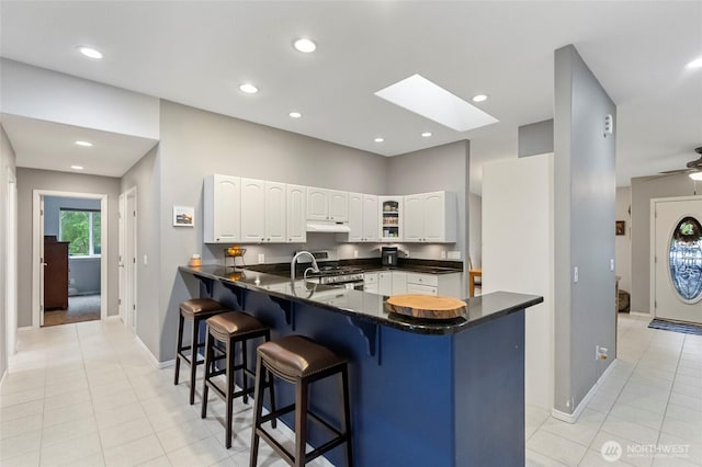 1555 Silver Lake Rd, Oak Harbor, WA 98277 - kitchen featuring under cabinet range hood, a breakfast bar, white cabinetry, a peninsula, and baseboards