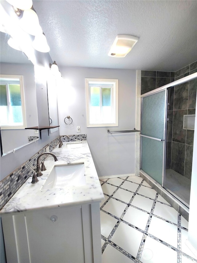 bathroom featuring a shower stall, double vanity, and a textured ceiling