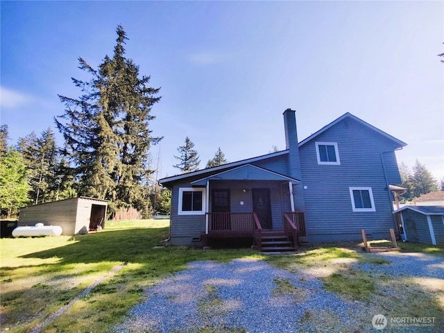 view of front of house featuring a chimney, a front lawn, an outdoor structure, crawl space, and covered porch