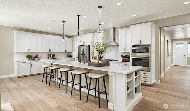 13513 100th St NE Unit 215, Lake Stevens, WA 98258 - kitchen featuring wall chimney exhaust hood, stainless steel appliances, light wood-style flooring, a large island, and a textured ceiling