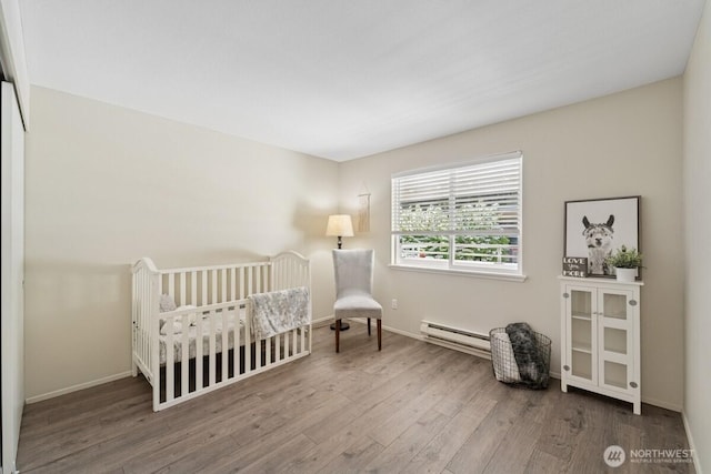bedroom featuring baseboard heating, wood finished floors, baseboards, and a crib