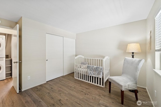 bedroom with estacked washer and dryer, wood finished floors, a closet, and baseboards