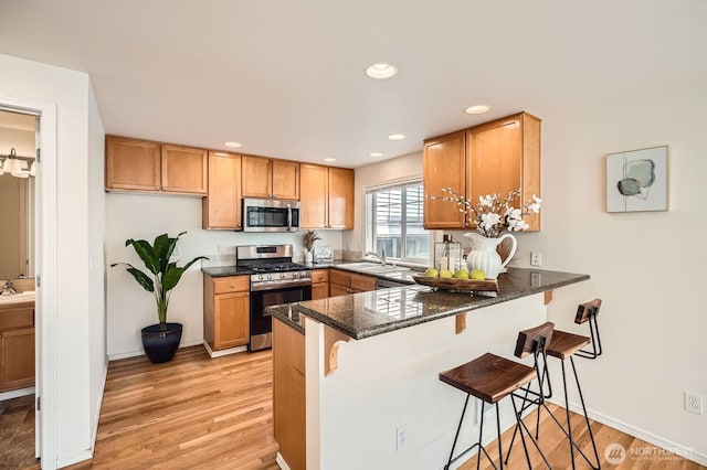 kitchen with stainless steel appliances, dark stone counters, light wood-style floors, a peninsula, and a kitchen bar