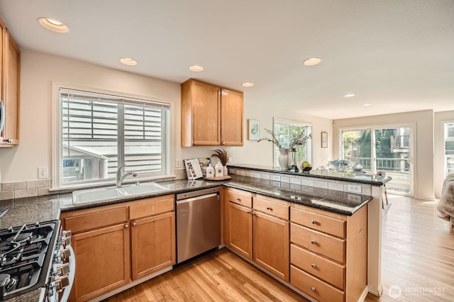 kitchen with appliances with stainless steel finishes, a peninsula, a sink, dark countertops, and light wood finished floors