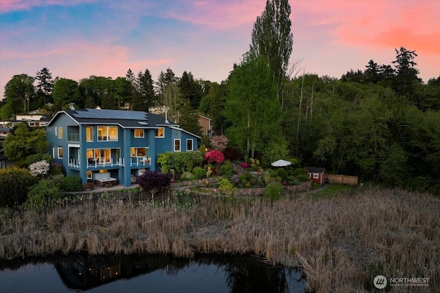 back of property at dusk with solar panels and a water view