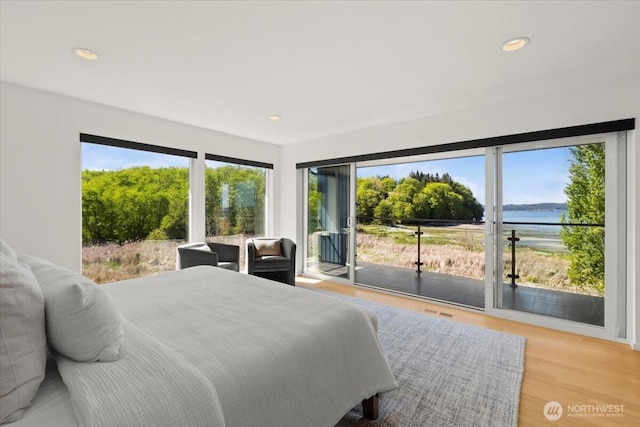 bedroom with access to exterior, a water view, light wood-style flooring, and recessed lighting