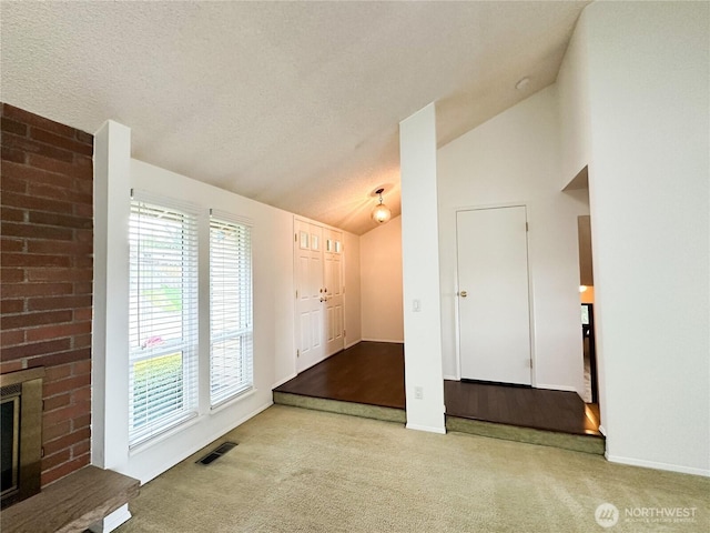 foyer with lofted ceiling, carpet, baseboards, a brick fireplace, and a textured ceiling