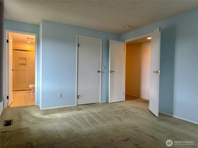 unfurnished bedroom with carpet floors, a textured ceiling, baseboards, and ensuite bathroom