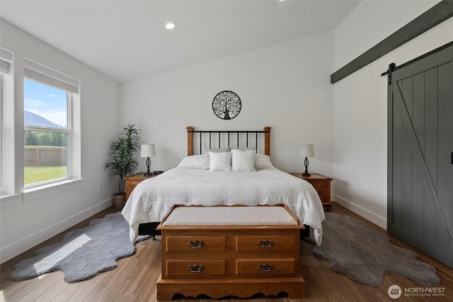 bedroom with a barn door, baseboards, wood finished floors, and recessed lighting