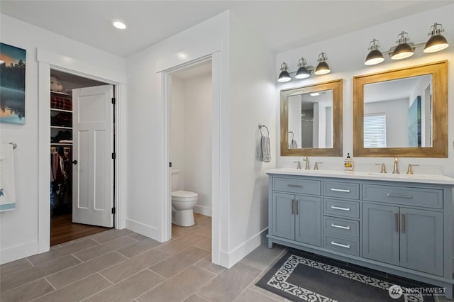 bathroom with toilet, double vanity, a spacious closet, baseboards, and recessed lighting