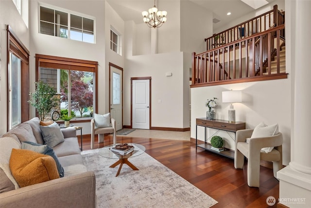 living area with wood finished floors, a towering ceiling, a chandelier, and baseboards