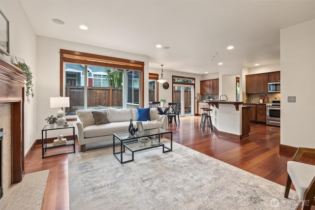 living area with dark wood finished floors, recessed lighting, a brick fireplace, and baseboards