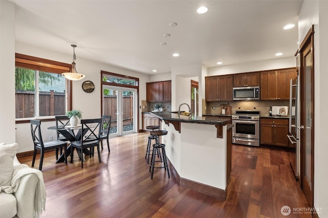 kitchen with appliances with stainless steel finishes, a breakfast bar area, dark wood-type flooring, decorative backsplash, and recessed lighting