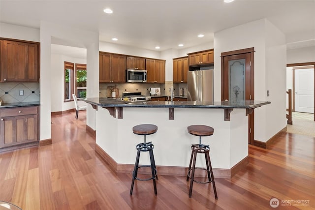 kitchen featuring stainless steel appliances, light wood-style floors, a breakfast bar area, backsplash, and recessed lighting