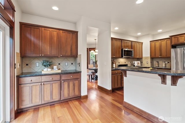 kitchen featuring appliances with stainless steel finishes, a kitchen breakfast bar, light wood-style floors, tasteful backsplash, and recessed lighting